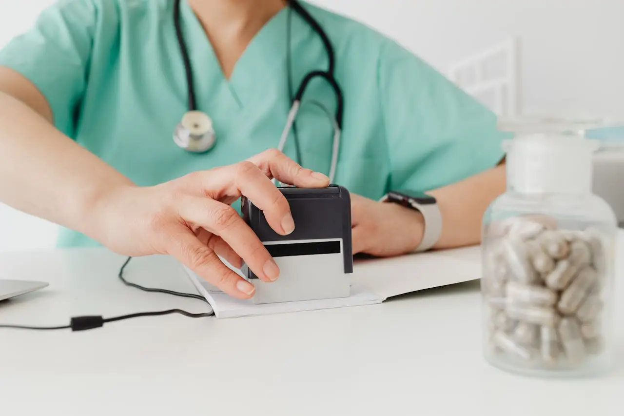 Close-up of a doctor stamping a prescription with a bottle of pills on a desk.